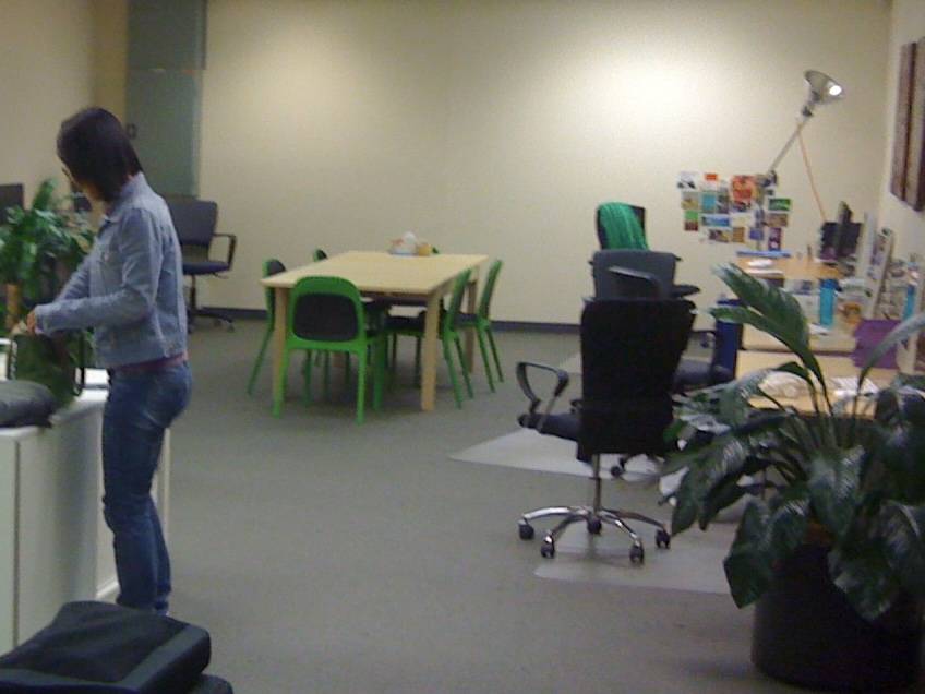 An open plan studio with desks down one wall and a table in the middle. A woman stands to one side.